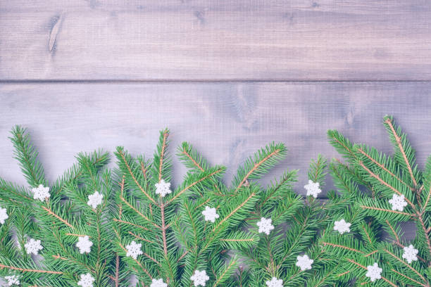 istock Winter composition with copy space. The branches of the Christmas tree are decorated with small snowflakes and beautifully laid out on a wooden background. Festive layout with place for text. 1073058310