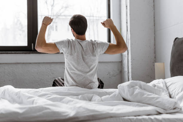 istock back view of young man in pajamas stretching while sitting in bed 1073071198