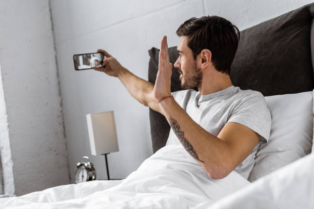 istock handsome young man chatting with smartphone and waving hand in bed 1073071242