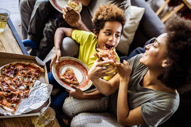 흑인 어머니의 볼 위에 피자 집에서 그녀의 딸을 먹이. - pizza eating african descent lunch 뉴스 사진 이미지