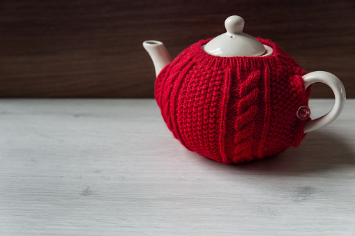 Red sweater cozy teapot on wooden background