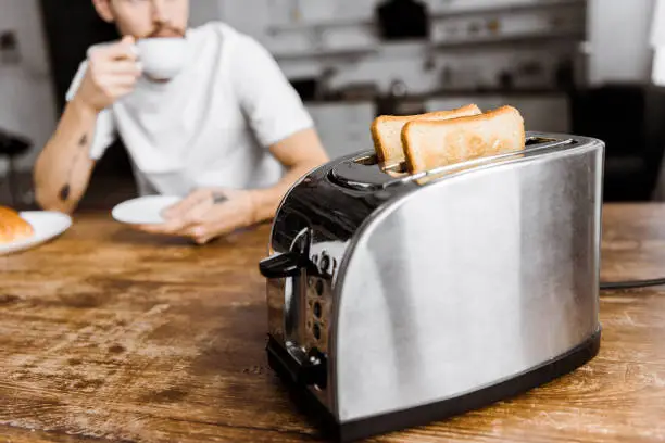 Photo of cropped shot of young man drinking coffee at home with toaster on foreground