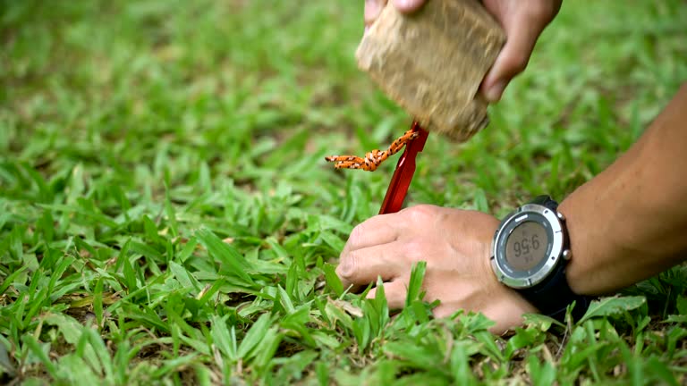 Man using rock to knock tent peg into ground.