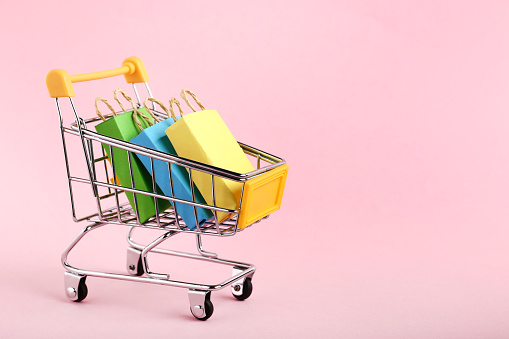 Small paper shopping bags with shopping cart on pink background