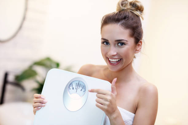donna felice che tiene le bilance del bagno in bagno - weight women medicine lost foto e immagini stock