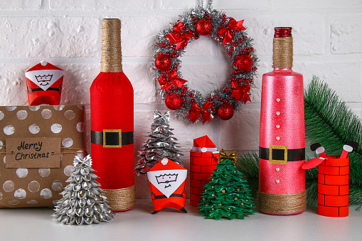 Diy bottle Santa. Guide on the photo how to make the decor of the bottle in the form of Santa Claus of red paint or paper and hemp rope. Handmade The decor. Gift wrapping.