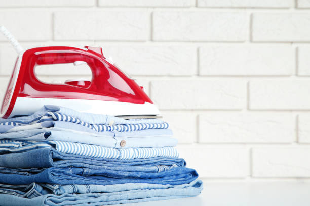 istock Stack of folded clothes with electric iron on brick wall background 1073137232