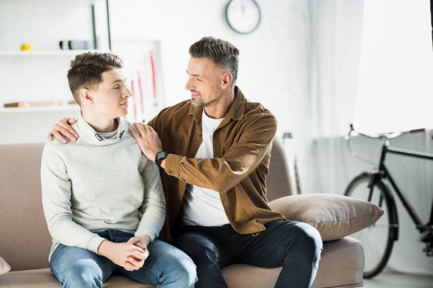 istock father hugging teen son on sofa at home 1073151510