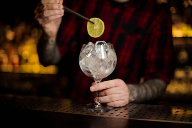 istock Bartender adding lime slice to the cocktail glass full of ice cubes 1073163824