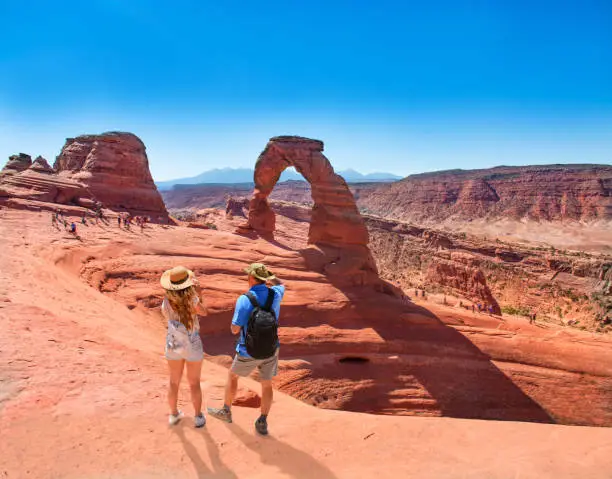Couple on vacation hiking trip. Man and woman standing on top of the mountain looking at beautiful view. Delicate Arch,  Moab, Utah, Arches National Park.