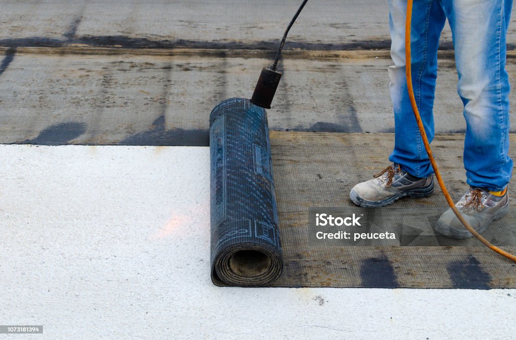 Roofer installing rolls of bituminous waterproofing membrane for the waterproofing of a terrace Rooftop Stock Photo