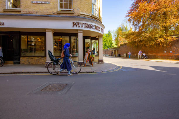 Young Muslim women pushing a bicycle through Cambridge outside a Patisserie.