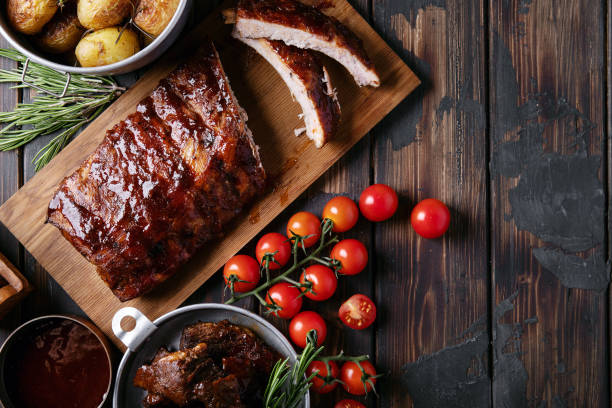 Home made pork and beef ribs Home made pork and beef ribs, glazed with barbecue sauce served with baked rosemary potatoes, herbs and tomatoes, decorated with napkins over a rustic wooden background. Top View. Copy Space rib stock pictures, royalty-free photos & images