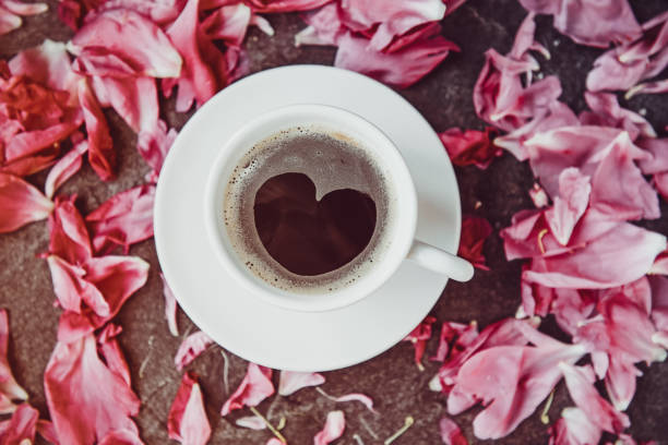 flache laien tasse kaffee mit herz form muster mit leichten rosa pfingstrose blüten auf schwarzem stein umgeben. valentinstag, guten morgen-konzept. kalten tönen. ansicht von oben, nahaufnahme. - comfort food high angle view directly above close up stock-fotos und bilder