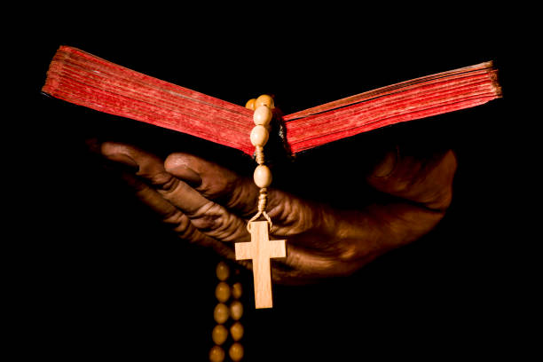istock Hand holding an open book with a rosary, isolated on a black background 1073195420