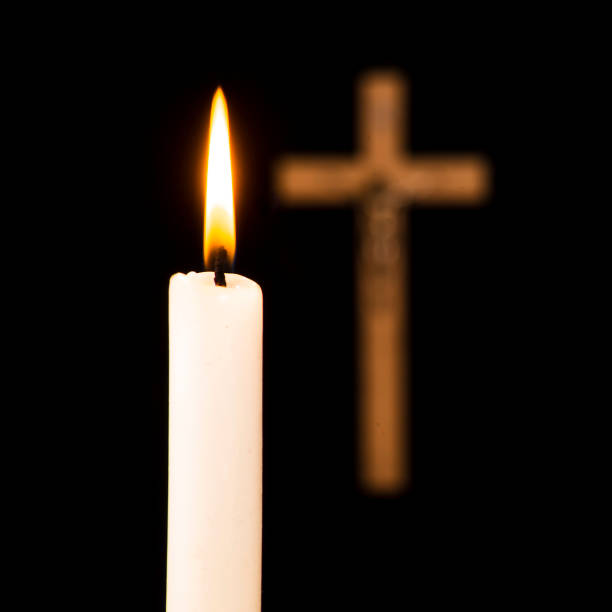 istock Lit candle with a crucifix in the background, isolated on a black background 1073196272