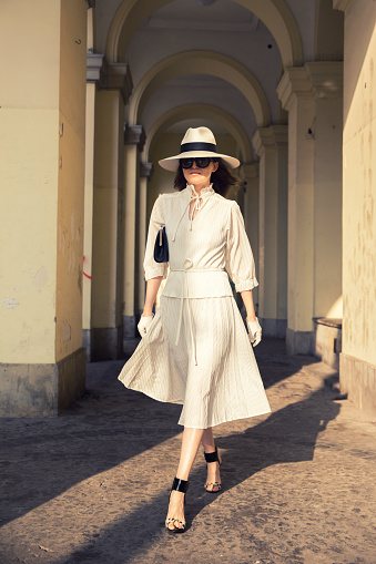 Elegant woman walking around city center. Wearing matching gloves, hat and dress