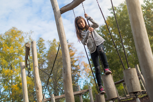 A girl climbs an obstacle course at a playground on an autumn day.