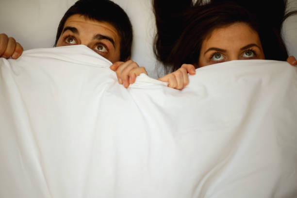 istock Frightened couple with eyes wide open under blanket 1073224954