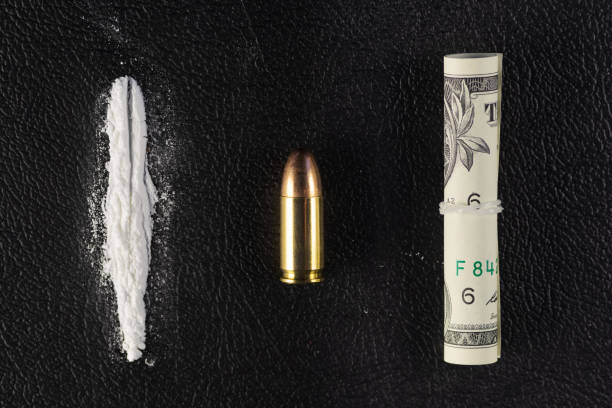 A line of cocaine powder, single bullet and dollar bill scroll on black surface stock photo