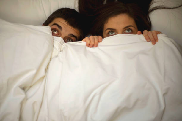 istock Frightened couple with eyes wide open under blanket 1073225988