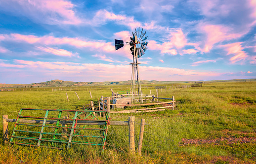 Pastel pink sunset sky behind old wooden windmill in western Wyoming.