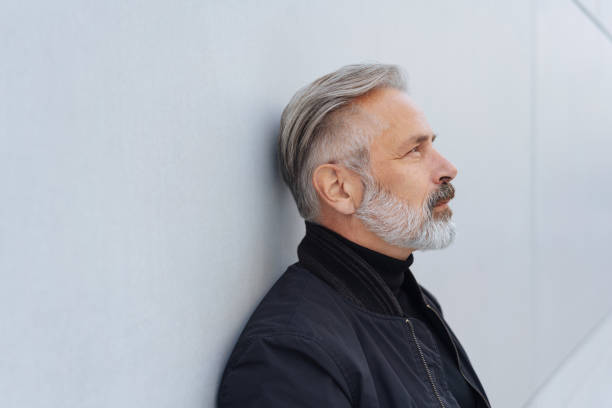 istock Mature thoughtful bearded man standing by wall 1073250244