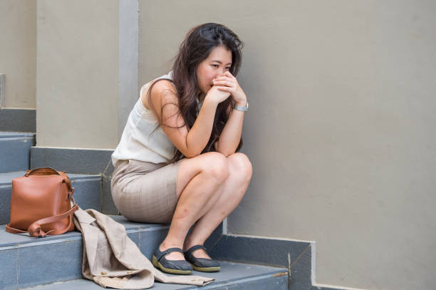 young depressed and desperate Asian Korean business woman crying alone sitting on street staircase suffering stress and depression crisis being victim of mobbing or fired losing her job stock photo
