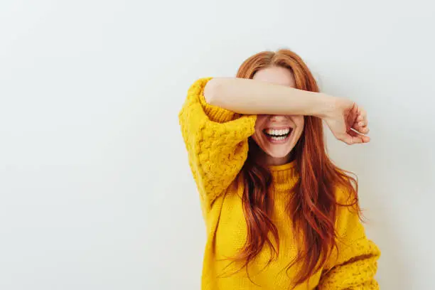 Photo of laughing woman covering her eyes with her arm