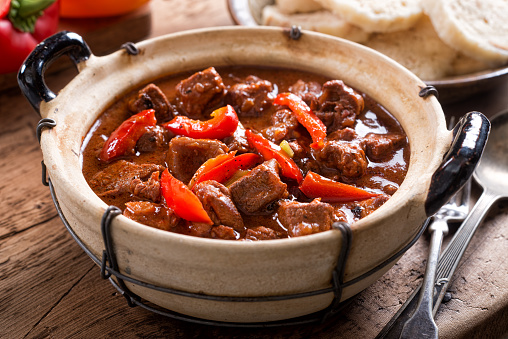 A bowl of delicious authentic Hungarian goulash with bread dumplings and red pepper garnish.