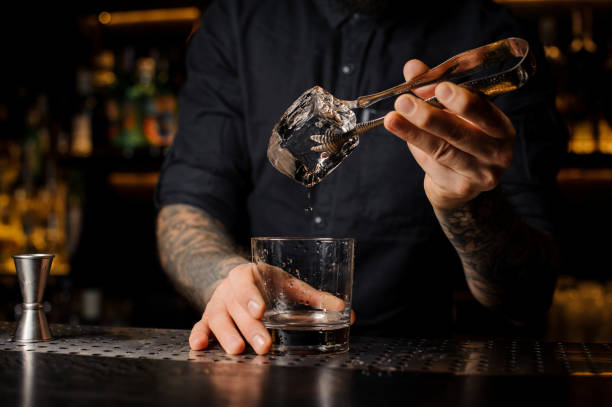 istock Tattooed mixologist putting an ice cube into a cocktail glass 1073297464