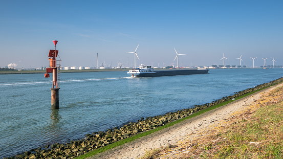 Ship sailing on the New Waterway along industries and wind turbines in the direction of the North Sea. This is the access route for large seagoing vessels from the North Sea to the port of Rotterdam.