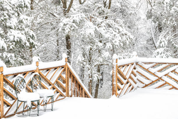 foresta, casa innevata, ponte di legno domestico con due sedie in ghisa, nevica, fiocchi di neve che cadono, tempesta di neve, tempesta, alberi nel cortile, cortile anteriore, ringhiera, recinzione in inverno con nessuno - deck front or back yard landscaped house foto e immagini stock