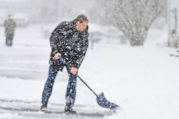 defokussierten junger mann, männlich im winter mantel reinigen, schaufeln auffahrt, straße von schnee in schweren schneesturm geschneit, holding, schaufel, wohnhäuser, schneeflocken fallen - snow digging horizontal people stock-fotos und bilder