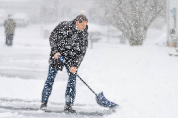 дефокированный молодой человек, мужчина в зимнем пальто уборка, лопатой подъездной путь, улица от снега в сильный снег метель, держа лопату, - snow digging horizontal people стоковые фото и изображения