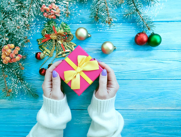 istock women's hands, gift box, Christmas tree branch on a wooden background 1073359082
