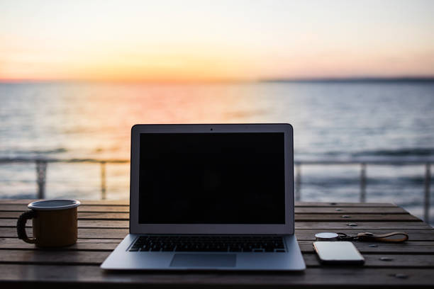 istock Laptop, coffee and phone on workspace and sea at sunset background 1073389324