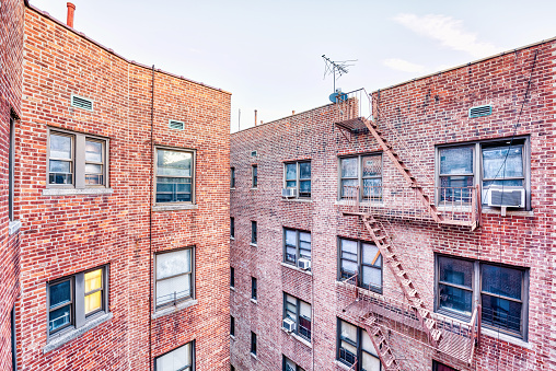 Brick apartment condo building roof exterior architecture in Fordham Heights center, Bronx, NYC, Manhattan, New York City with fire escapes, windows, ac units in morning, satellite dish, antenna, USA