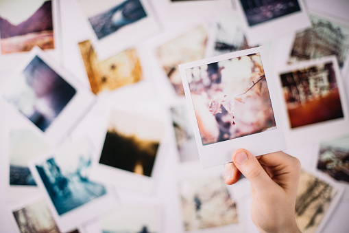 A hand holding a polaroid over a bunch of other polaroids in the blurred background