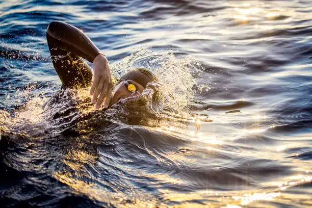 Side view of a male triathlete swimming in the sea that is reflecting the sunlight.