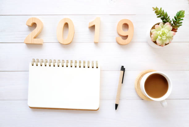 istock 2019 wood letters, blank notebook paper and coffee on white table background, 2019 new year mock up, template with copy space for text, top view 1073406864
