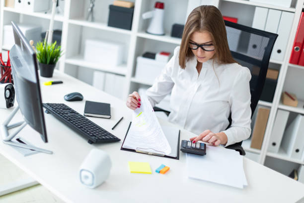 istock Young girl sitting at the table and working with a computer, documents and calculator 1073415600