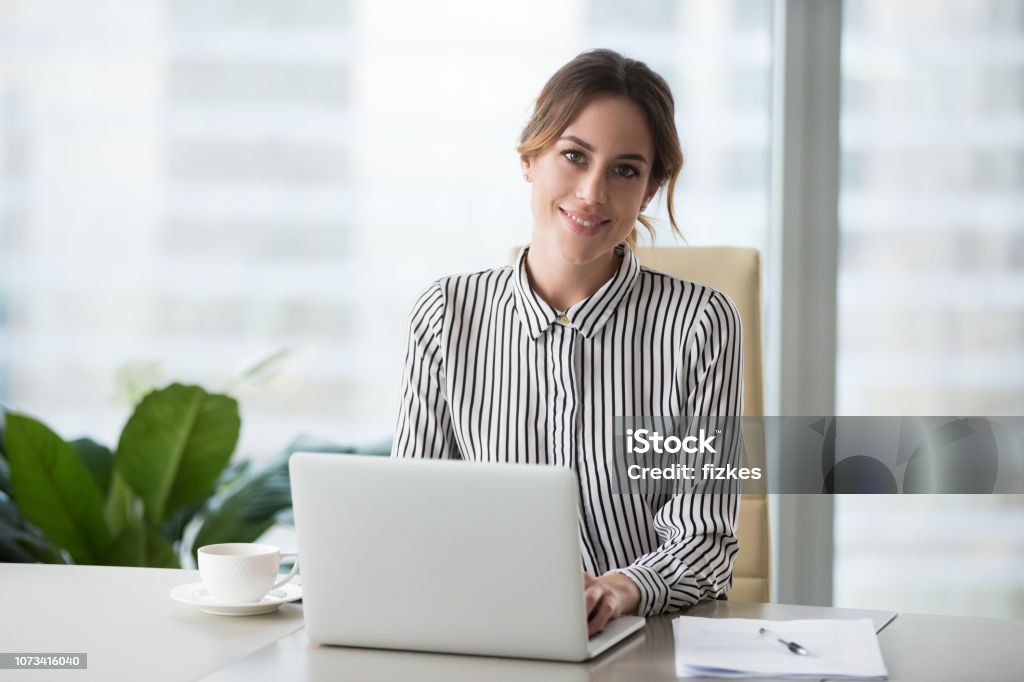 Head shot portrait of confident businesswoman at workplace Head shot portrait of confident businesswoman at workplace, smiling woman employee sitting behind laptop and looking at camera. Staff at work. Businesswoman Stock Photo