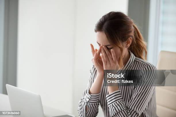 Tired Young Woman Massaging Nose Bridge At Workplace Stock Photo - Download Image Now