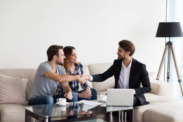 Young couple, family making deal with Real Estate Agent, interior designer Young couple, family at meeting with Real Estate Agent, interior designer, decorator, landlord making deal. Husband handshaking with man in suit. Concept of meeting with client, customer brokers stock pictures, royalty-free photos & images