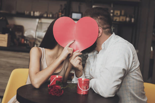 istock Young charming couple hides behind paper heart 1073417368