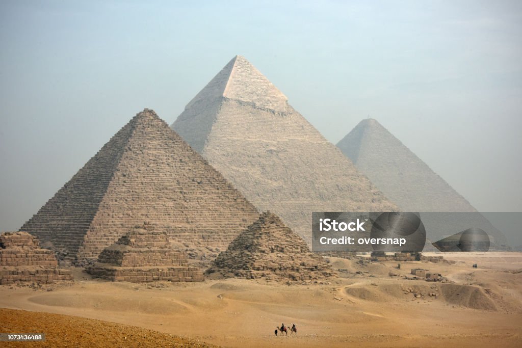 Pyramids A distant camel caravan passes the majestic pyramids at Giza in Cairo at dusk. Egypt Giza Pyramids Stock Photo