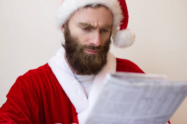 istock Serious guy wearing Santa costume and reading newspaper 1073442880