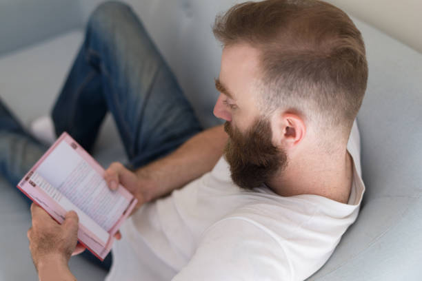 istock Concentrated man focused on content of book sitting on sofa 1073442952