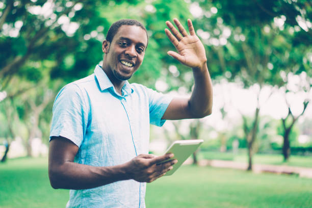 istock Cheerful friendly young African man with tablet waving hand 1073444768